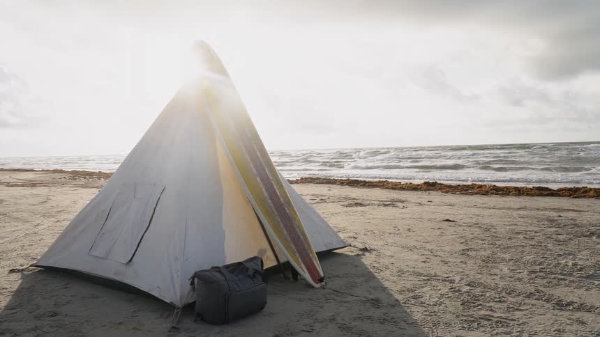 Surf boarding leaning against tent on ocean beach
