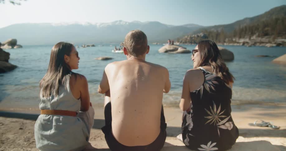 Three people sit on the beach as the waves roll in