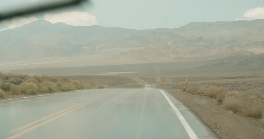 A car drives on a rural road in the rain