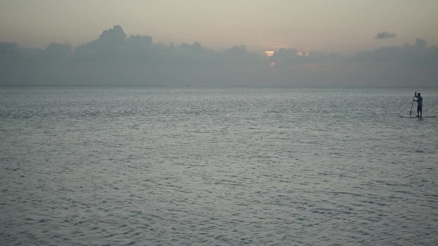 Man is paddle boarding on body of water at sunset