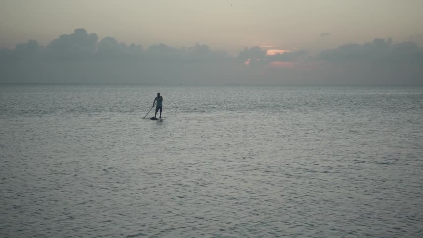Person stands on a surfboard paddling in the ocean