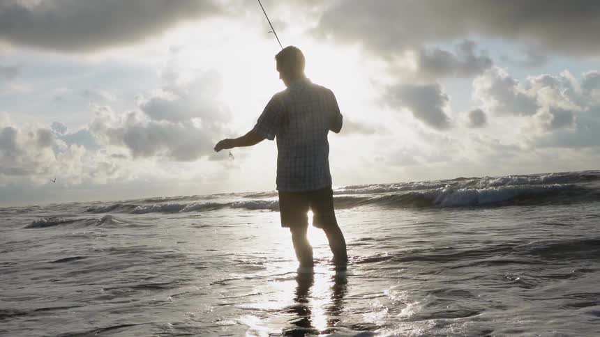 A man fishes on a beach on a cloudy day