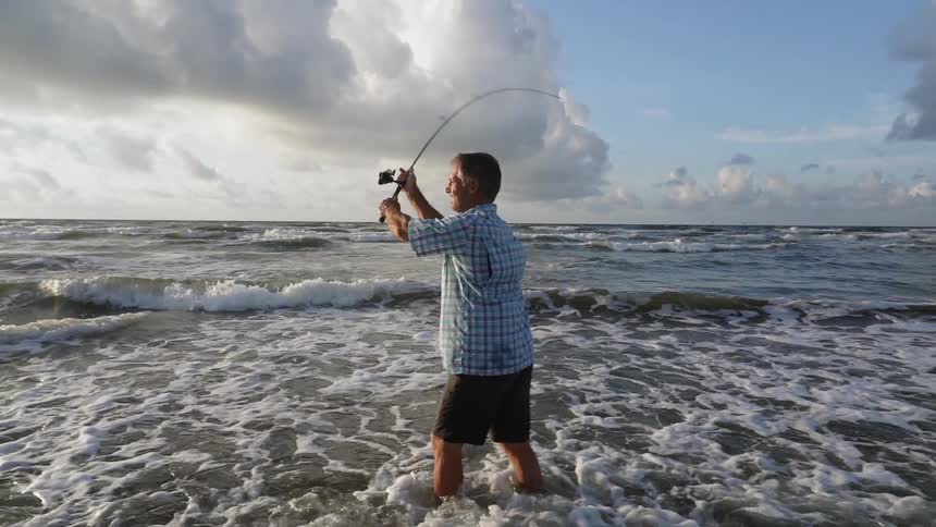 A man fishes on a beach on a cloudy day