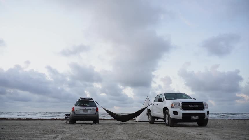 A hammock is strung between two vehicles on a beach