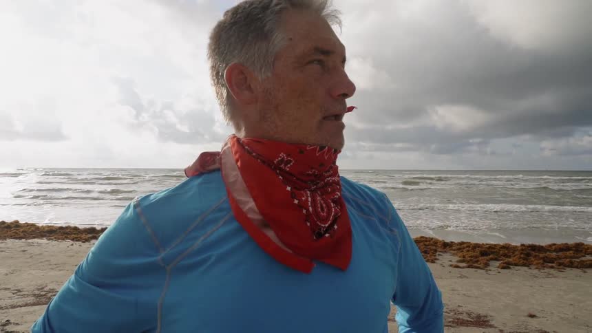 A man stands on a beach with a handkerchief tied around his neck
