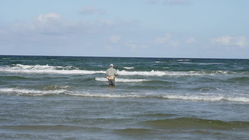 A man is walking into the surf fishing