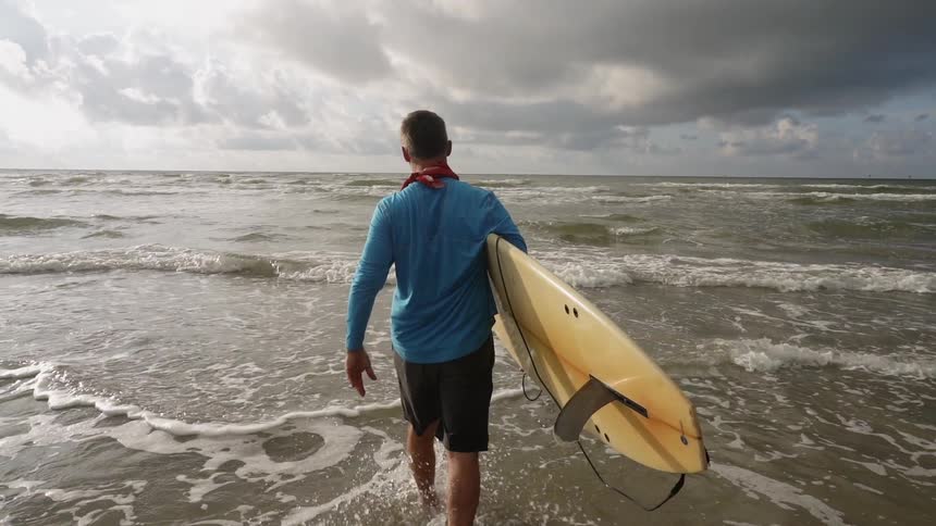 A man carries a surfboard into the ocean