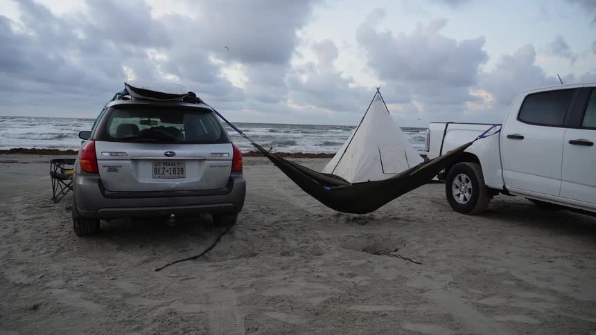 A hammock is strung between two vehicles on a beach