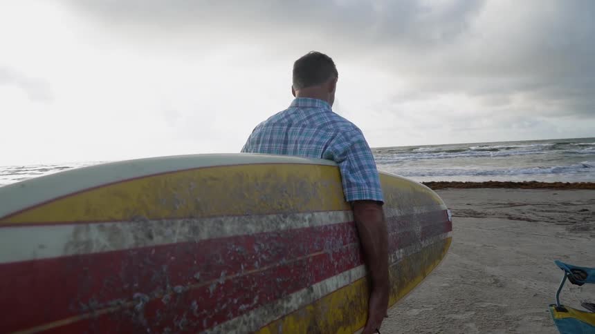 A man carries his surfboard towards the water