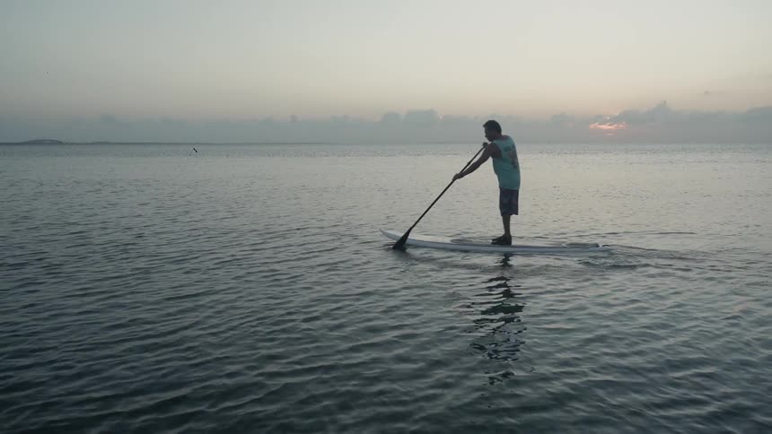 A man is paddling on a surfboard