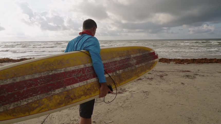 A man carries his surfboard on the coast