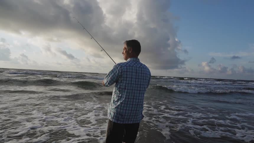 A man fishes on a beach on a cloudy day