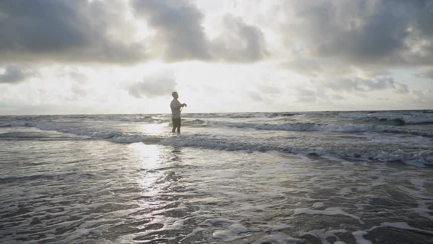 A man fishes on a beach on a cloudy day