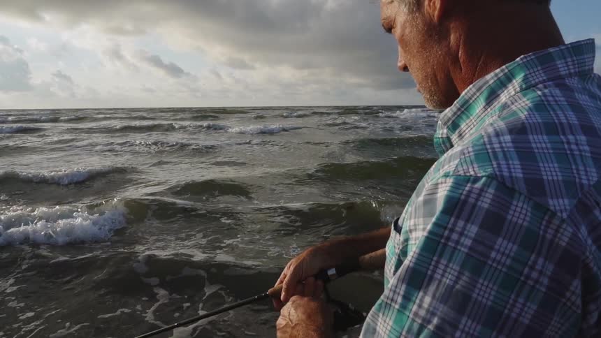 A man fishes on a beach on a cloudy day