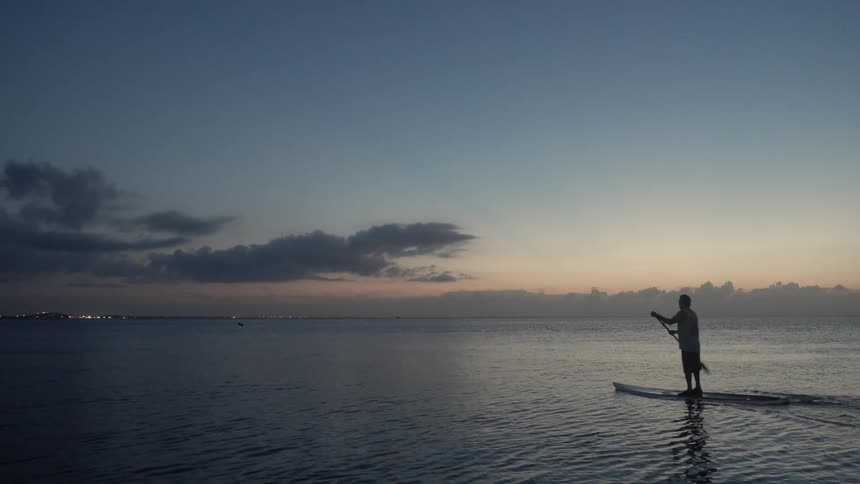 A man paddleboards on a lake at sunset