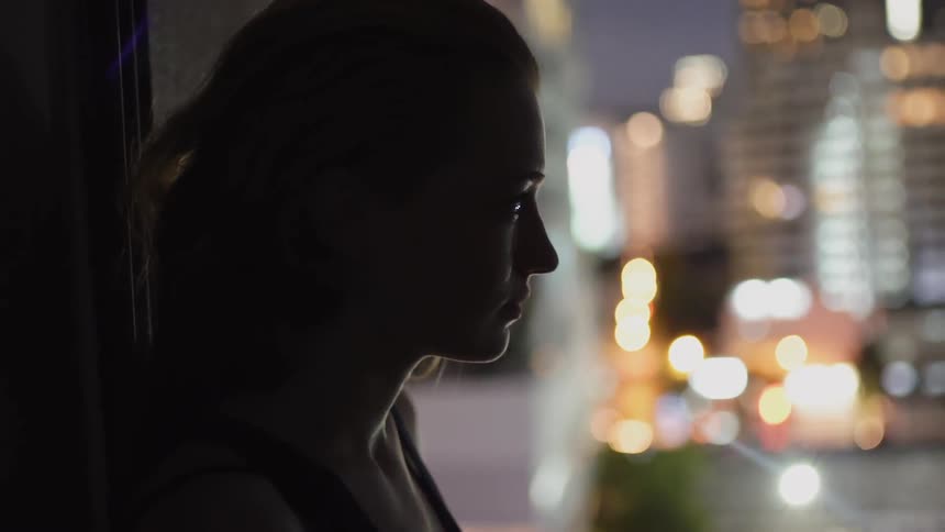 Woman stands looking out a window at the city down below