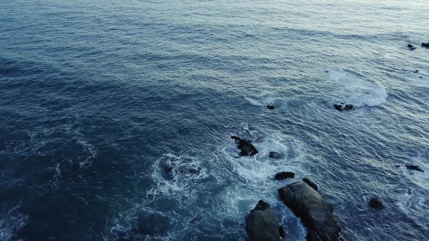 The waves crash against the rocks on a sunny day