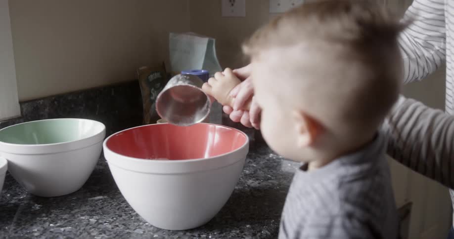 Woman helps a child pour flour into a large bowl in a kitchen