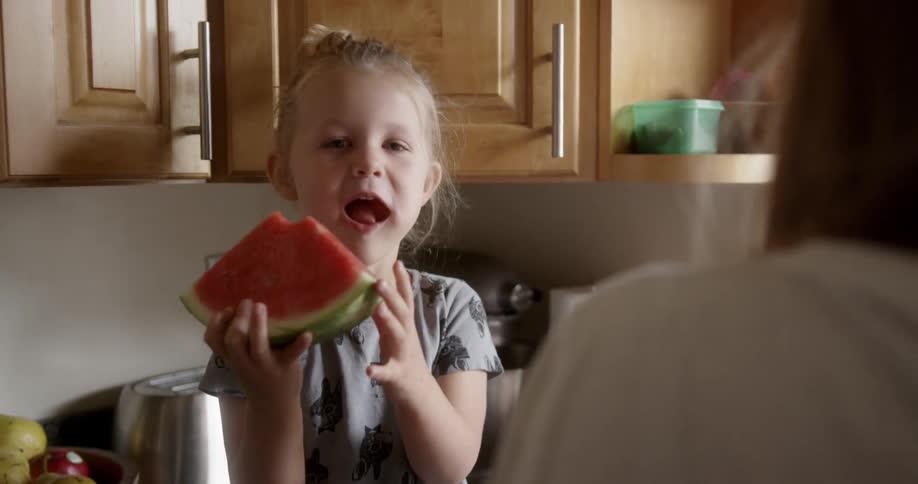 A child is eating some watermelon in the kitchen