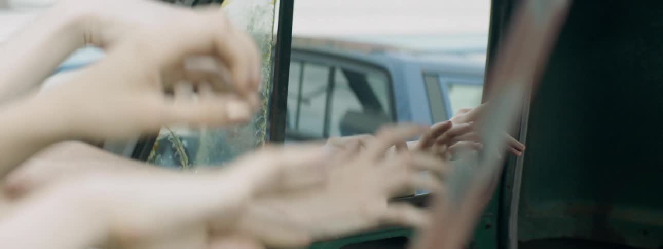 People are moving their hands in the open windows of a derelict vehicle in daylight