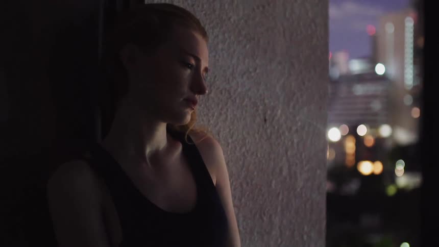 Woman leans against a large pillar looking out at the city