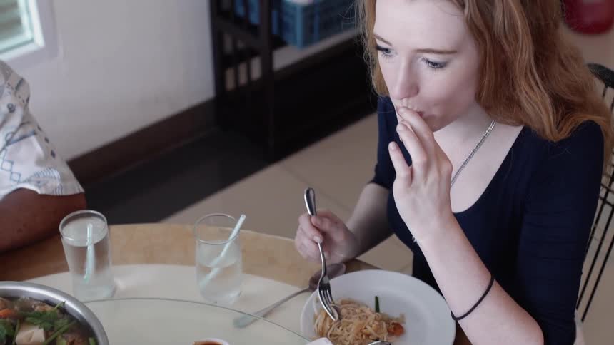 A woman is eating Asian food at a table with a hot pot inside in daylight