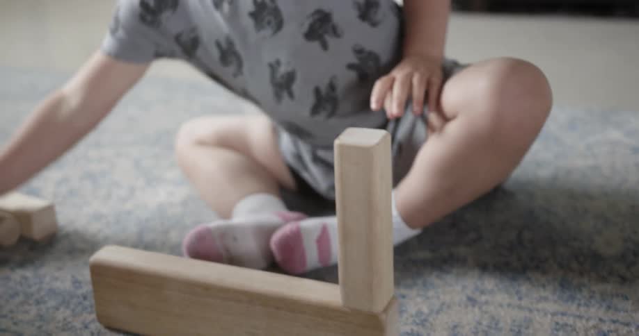 A young girl plays with wood blocks on a rug