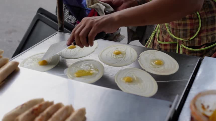 A vendor is cooking eggs at a cart outside in an asian city in daylight