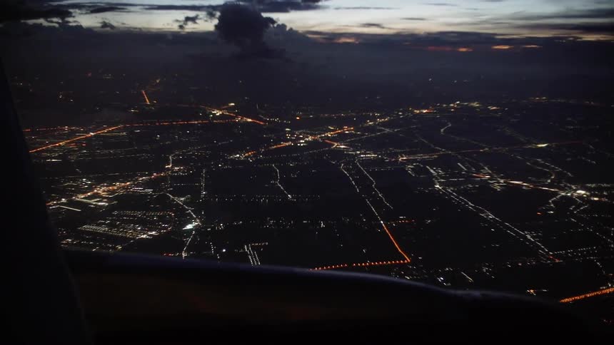 An airplane flies over a city at dusk