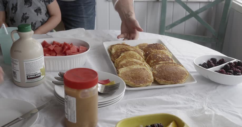 Man sets plate of pancakes on breakfast table
