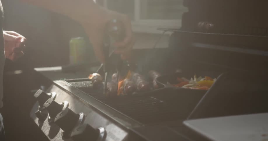 Man is turning hot dogs on grill