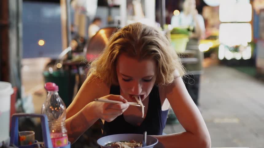 Woman eats noodles with chopsticks in a restaurant
