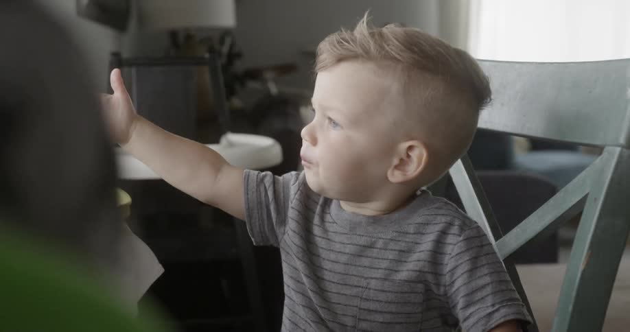 A toddler boy is eating a berry at a kitchen table in daylight