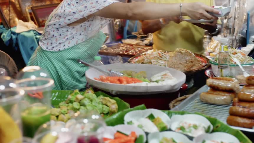 A woman in an asian market is handing a dish of food to a customer