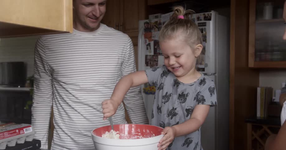 Parents are watching as their daughter mixes batter in a bowl inside in daylight