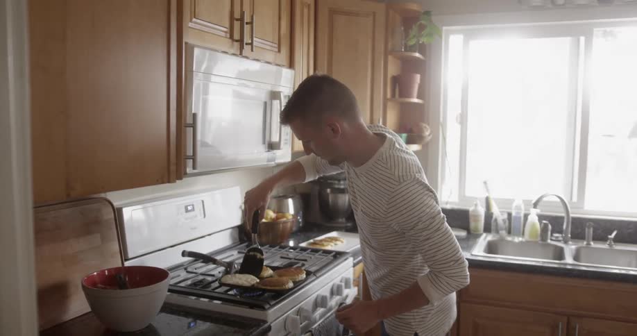 A man is cooking pancakes inside a kitchen in daylight