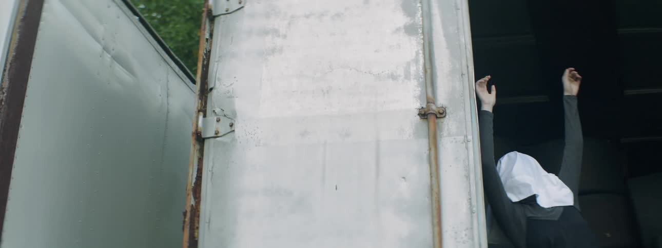 A person dances next to a metal door with bag on their head