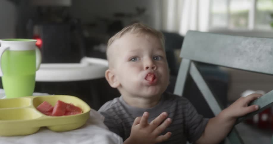 A boy picks up a piece of watermelon and eats it