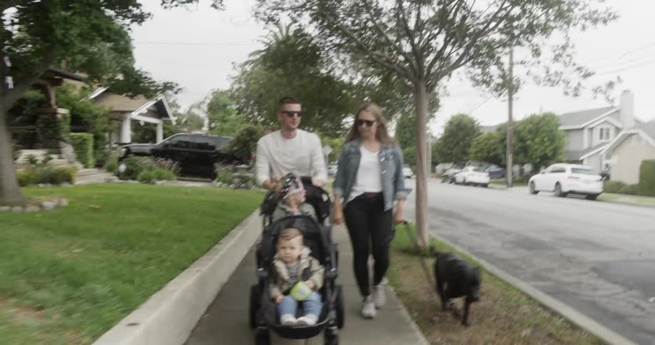 A mother and father walk their dog and children outside