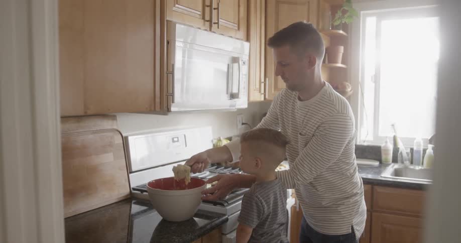 Toddler watches as a man scoops batter from a bowl and puts it on a pan