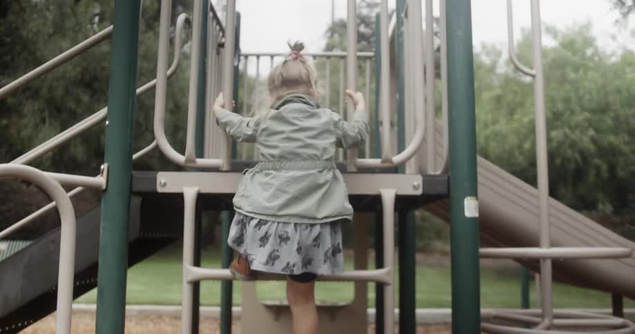 A young girl climbs up a playground ladder