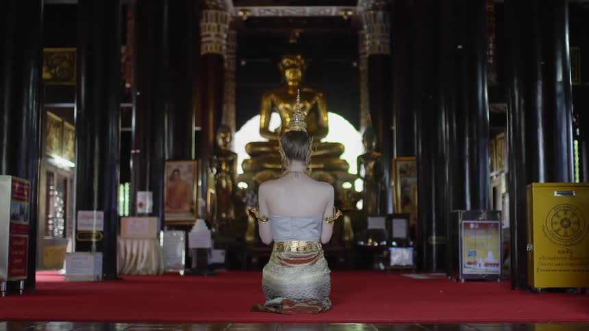 A woman kneels in front of a statue