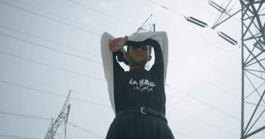 A man slowly raises his arms beneath power lines