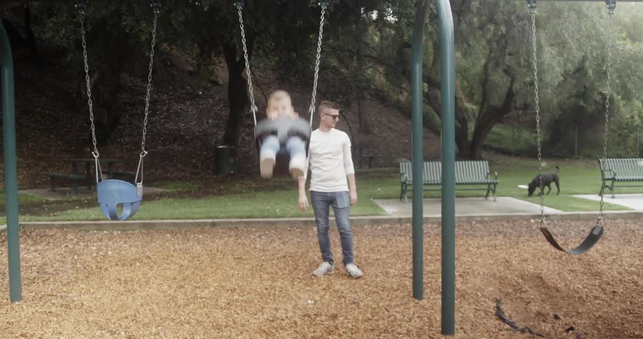 A father pushes his son on a swing at a park