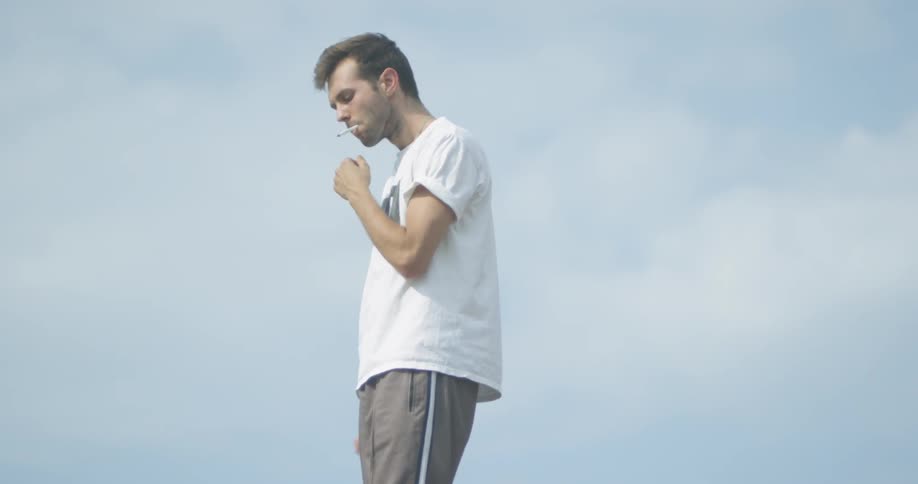 Man is outside lighting and smoking cigarette on cloudy day