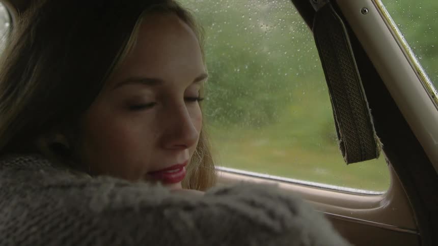 A blonde woman riding in a vehicle that has raindrops on the windows