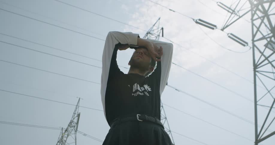 A man slowly raises his arms beneath power lines