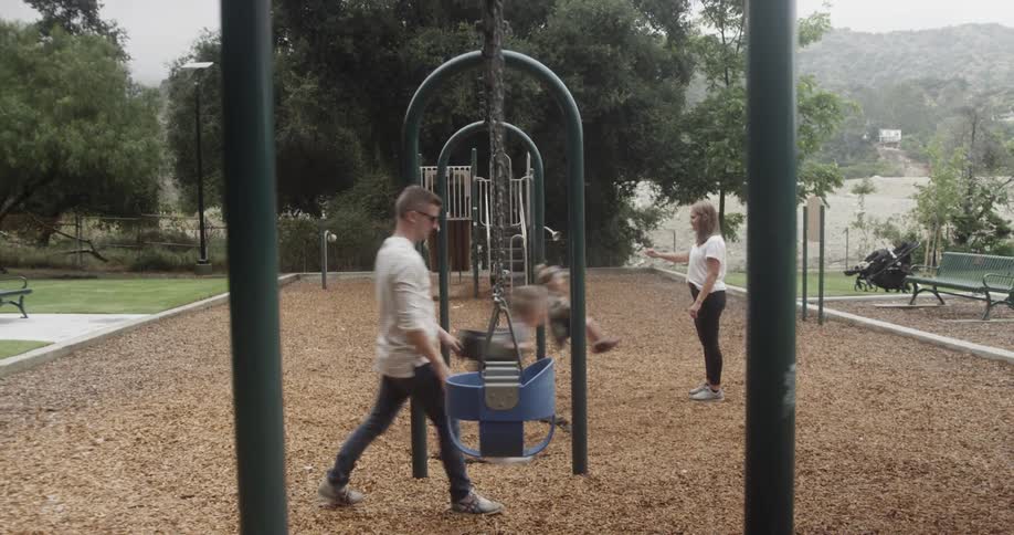 Mother and father are pushing their children on park swing set