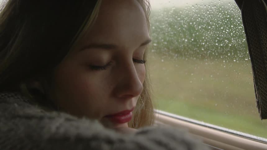 A blonde woman traveling in a vehicle that has raindrops on the windows