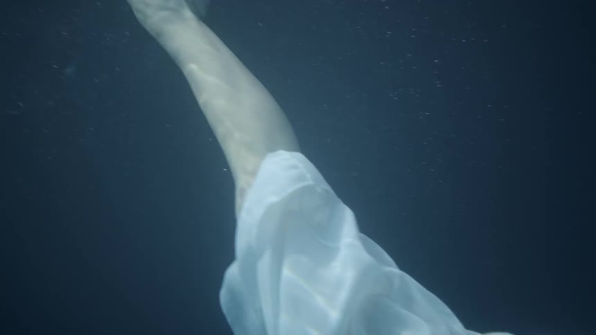 Woman wearing a dress floats under the water